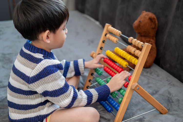 A young child uses a colorful abacus for counting.